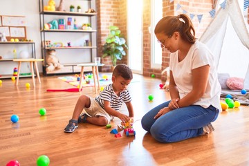 Fototapeta premium Beautiful teacher and toddler boy playing with train at kindergarten