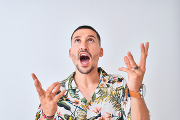 Young handsome man wearing Hawaiian summer shirt over isolated background crazy and mad shouting and yelling with aggressive expression and arms raised. Frustration concept.