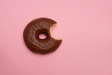 Delicious bitten doughnut with chocolate glaze on soft pink paper background