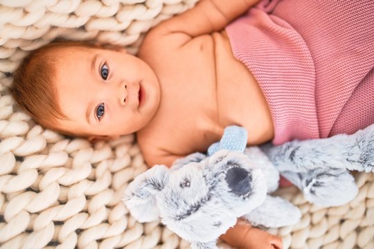 Adorable baby lying down over blanket on the sofa smiling happy at home. Newborn with smile on face relaxing and resting with teddy bear comfortable