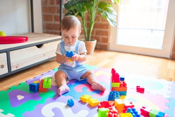 Beautiful toddler sitting on puzzle carpet playing with building blocks at kindergarten