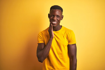 Young african american man wearing casual t-shirt standing over isolated yellow background touching mouth with hand with painful expression because of toothache or dental illness on teeth. 