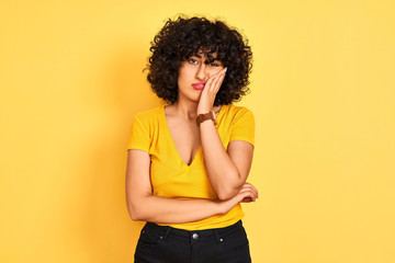 Young arab woman with curly hair wearing t-shirt standing over isolated yellow background thinking...