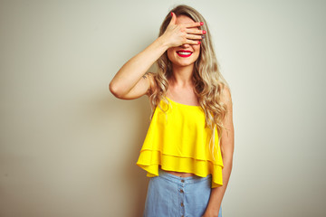 Young beautiful woman wearing yellow t-shirt standing over white isolated background smiling and laughing with hand on face covering eyes for surprise. Blind concept.