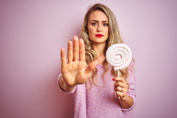 Young beautiful woman eating sweet candy over pink isolated background with open hand doing stop...