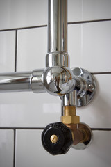 Chrome towel radiator with brass control valve on a tiled wall of white brick tiles