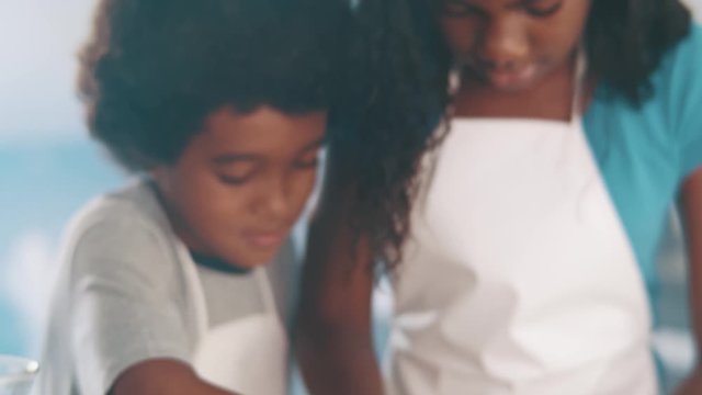 Young family cooking food in kitchen. Happy Little girl with her mother mixing batter. Mother and Little boy preparing the dough. Happy family in the kitchen and junior chef Concept. Cinematic 4k.