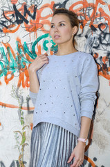 A young girl in a silver blouse with rhinestones on the background of a textured wall with graffiti elements. Happy girl on vacation.