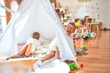 Adorable blonde twins playing inside tipi around lots of toys at kindergarten