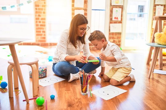 Beautiful teacher and toddler drawing using digital board around lots of toys at kindergarten