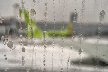 Defocused airplanes view glass with drops of water. Raindrops on airplane window by the runway.