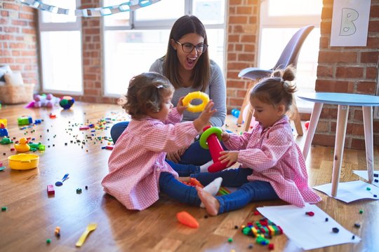 Young beautiful teacher and toddlers wearing uniform building pyramid using hoops at kindergarten