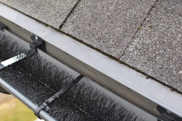 Plastic guard brush in new dark grey plastic rain gutter on asphalt shingles roof.