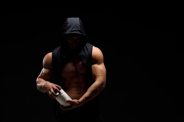 Naklejka na ściany i meble Muscular bodybuilder with jar of protein on a dark background. Sports nutrition. Bodybuilding nutrition supplements, sport, workout, healthy lifestyle concept.