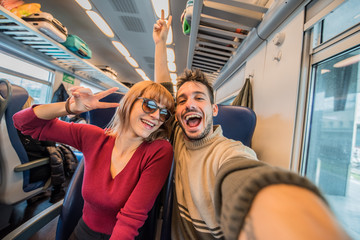 Excited couple sitting by the train taking selfie enjoying travel.