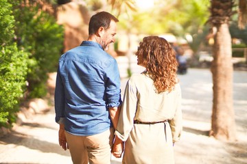 Middle age beautiful couple smiling happy and confident at town park. Walking with smile on face on backview