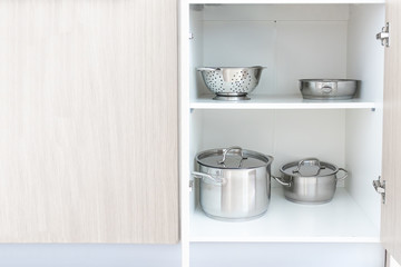 Storage of steel metal pans and other kitchenware, cookware utensils in cupboard of modern kitchen,...
