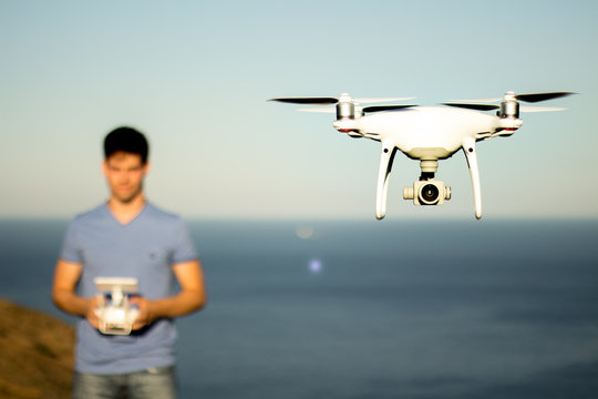 Drone flying with a blurred operator behind, maritime landscape.