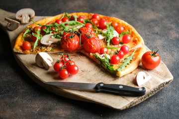 Traditional italian pizza with cherry tomatoes on a wooden shovel on a dark background.