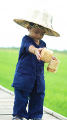 The cute boy in the nature, the outdoor lifestyle of Thai children sitting on a rice farm after rain before sunset, the children eat sticky rice, use the countryside in the way of the farmers concept