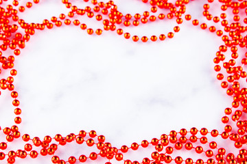 Red christmas beads on marble background. Christmas frame. Line of red beads garland on a white background. Top view. Copy space