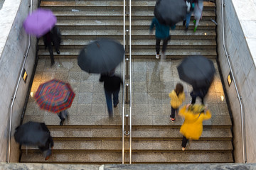 people on metro station stairs with umbrellas under rain