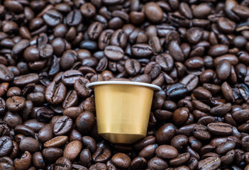 Golden coffee capsule on the dark roasted coffee bean.