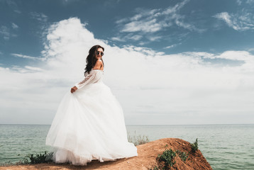 Beautiful bride in a white dress, in black glasses, stands on a rock