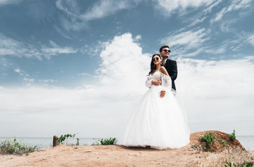  Loving newlyweds stand on a cliff by the ocean