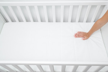 Woman hand pressing on white mattress. Mother checking hardness and softness of baby bed. Choice of...