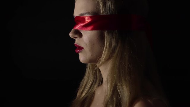 Portrait of the young woman blindfold with red ribbon. Sensual and fetish concept.