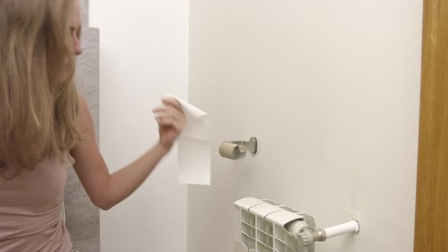 A woman is sitting on a toilet and running out of toilet paper