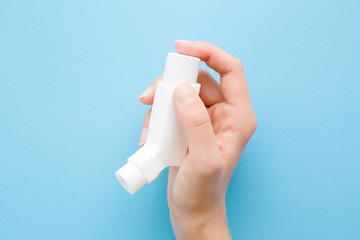 Woman hand holding white inhaler of asthma. Medical, pharmacy and healthcare concept. Point of view shot. Closeup. Pastel blue background. Top down view.