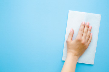 Woman hand wiping pastel blue desk with white paper napkin. General or regular cleanup. Closeup....