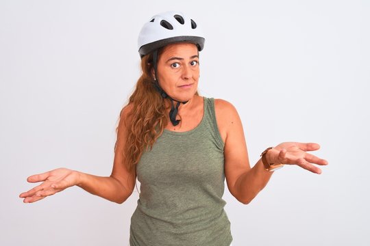 Middle age mature cyclist woman wearing safety helmet over isolated background clueless and confused with open arms, no idea concept.