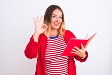 Young beautiful woman reading book standing over isolated white background doing ok sign with fingers, excellent symbol