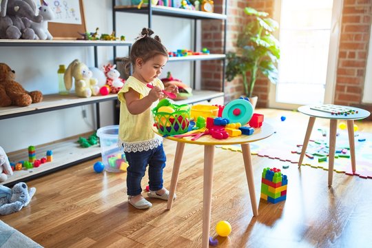 Beautiful toddler playing on the table with plastic vegetables and dishes at kindergarten