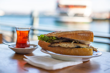 Istanbul fish sandwich. Burger with fried fish. Turkish tea with Balik Ekmek. Blurred background...