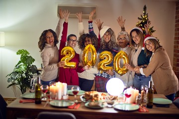 Beautiful group of women smiling happy and confident. Posing around christmas tree holding 2020 ballons at home