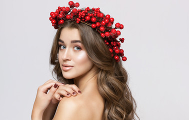 Portrait of a beautiful happy woman  with beautiful curly  hair and make up.She has a New Year's wreath of red berries on her head. Cosmetology skin care and make-up.