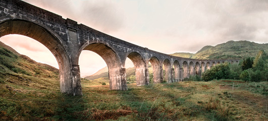 Glenfinnan Railway Viaduct. Harry Potter famous Glenfinnan viaduct, Scotland in cloudy weather and sunrise in the background. - obrazy, fototapety, plakaty