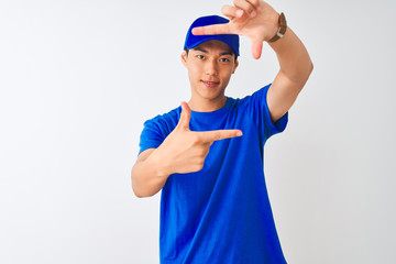Chinese deliveryman wearing blue t-shirt and cap standing over isolated white background smiling making frame with hands and fingers with happy face. Creativity and photography concept.