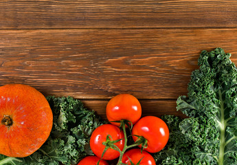 Tomatoes and a fresh leaf of kale cabbage with pumpkin on a wooden background. Top view.
