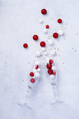 Two glasses for champagne and Christmas champagne bottle with sprinkles in the form of Christmas tree made of red and white toys balls decorated golden confetti on white background. Top view.