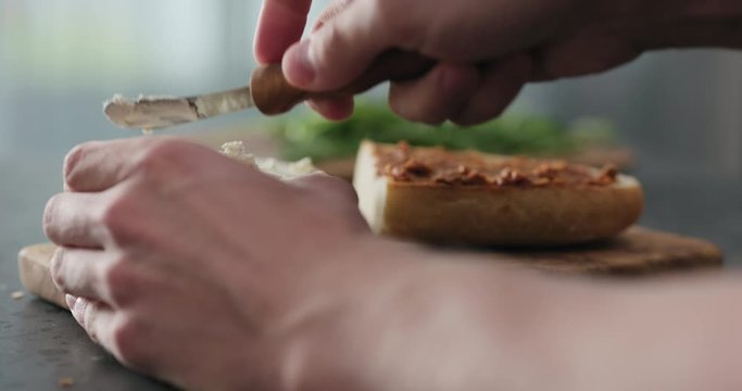Slow motion man spread cream cheese on ciabatta slice on olive board