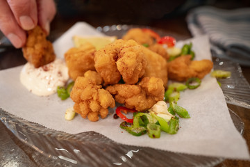 Crispy salt and pepper breaded squid with a lemon mayonnaise dip plus chilli, spring onion and corriander salad on a glass plate. A man is dipping one of the goujons.
