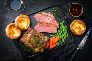 Traditional Commonwealth Sunday roast with sliced cold cuts roast beef with vegetable and Yorkshire pudding as top view on a modern design cast iron tray