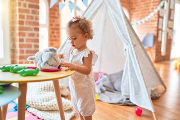 Beautiful caucasian infant playing with toys at colorful playroom. Happy and playful with stuffed animal at kindergarten.