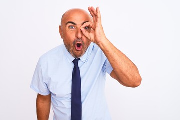 Middle age businessman wearing tie standing over isolated white background doing ok gesture shocked with surprised face, eye looking through fingers. Unbelieving expression.