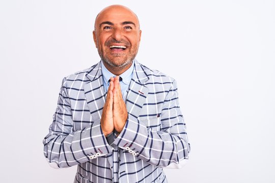 Middle age businessman wearing suit standing over isolated white background praying with hands together asking for forgiveness smiling confident.